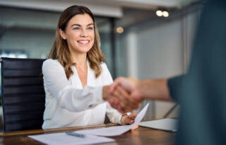Happy mid aged business woman manager handshaking at office meeting. Smiling female hr hiring recruit at job interview, bank or insurance agent, lawyer making contract deal with client at work.